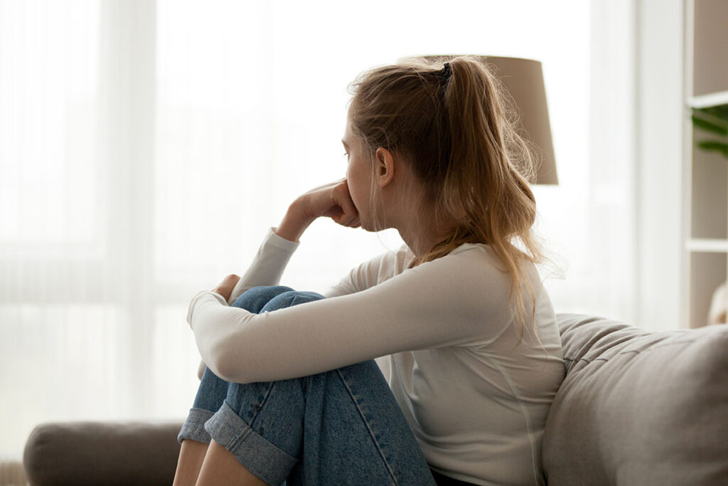 a person sits on a couch with their knees to their chest looking out a window wondering when is someone considered an alcoholic?